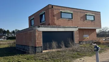 Rohbau eines modernen Einfamilienhauses mit Garage und großen Fenstern unter blauem Himmel.