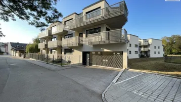 Modernes Mehrfamilienhaus mit Balkonen, Tiefgaragenzufahrt und Außenparkplätzen in sonniger Lage.