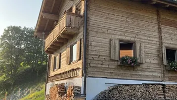 Traditionelles Holzhaus im alpinen Stil mit gestapeltem Brennholz und Blumenkästen an den Fenstern.