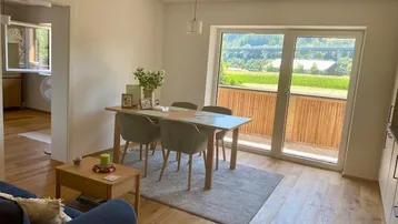 Helles Wohn- und Esszimmer mit Holzboden, Balkonzugang und weitem Blick ins Grüne.