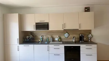 Moderne Einbauküche mit hellen Schränken, integrierten Geräten und einer Arbeitsplatte in dunklem Grau.