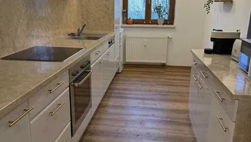 Funktionale Küche mit hellen Fronten, Laminatboden und Fenster, das Tageslicht hereinlässt.