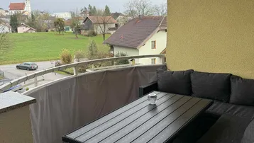 Möblierter Balkon mit Sitzgelegenheiten und weitem Blick über die Landschaft und ein Dorf.
