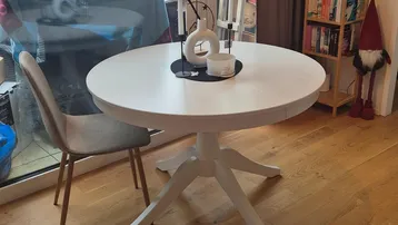Heller Wohnbereich mit Holzboden, einem runden Esstisch und Zugang zu einem Balkon oder einer Terrasse.
