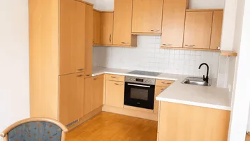 Funktionale Küche mit hellen Holzschränken, weißer Arbeitsplatte und integrierten Geräten.