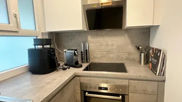 Moderne Küche mit grauen Arbeitsplatten, integriertem Backofen und Kochfeld sowie einem Fenster.