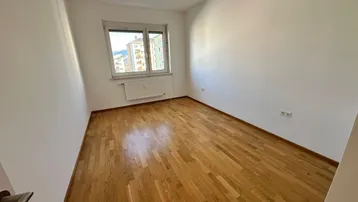 Gemütliches Schlafzimmer mit Parkettboden und Fensterblick, ideal für Ruhe und Entspannung.