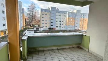Balkon mit Fliesenboden und Blick auf die umliegenden Wohngebäude und die Berglandschaft.