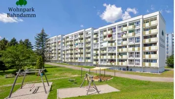 Großes Mehrfamilienhaus mit vielen Balkonen und einem Spielplatz im Vordergrund.