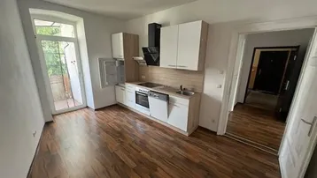 Moderne Einbauküche mit Holzoptik-Arbeitsplatte, weißen Schränken und Zugang zum Balkon.
