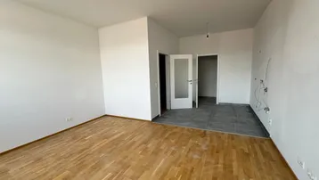 Heller, unmöblierter Wohnbereich mit Parkettboden und Übergang zu einem gefliesten Bereich.