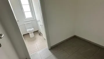 Kleines WC mit Fenster und hellen Fliesen, angrenzend an einen gefliesten Flur.