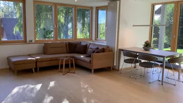 Helles Wohn- und Esszimmer mit großen Fenstern, Holzboden und bequemer Ledercouch.