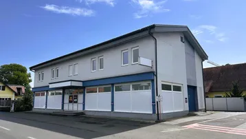 Ansicht des Geschäftsgebäudes mit hellgrauer Fassade, blauen Akzenten und großen Schaufenstern unter blauem Himmel.