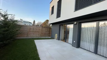 Moderne Terrasse mit Rasenfläche und Holzzaun, ideal für Entspannung im Freien.