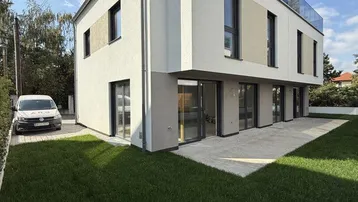 Moderne Neubau-Doppelhaushälfte mit Garten, Terrasse und Dachterrasse unter blauem Himmel.