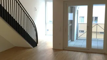 Heller Wohnbereich mit moderner Treppe, Holzboden und Zugang zu einem Balkon.