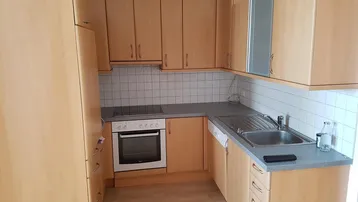 Funktionale Küche mit hellen Holzschränken, grauer Arbeitsplatte und weißen Wandfliesen.