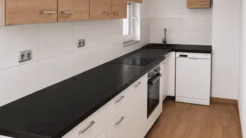 Moderne Küche mit hellen Holzschränken, schwarzer Arbeitsplatte und integrierten Geräten.