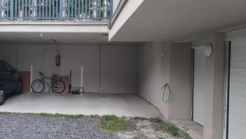 Überdachter Außenbereich mit Parkplätzen, Garagentoren und einem Balkon im Obergeschoss.