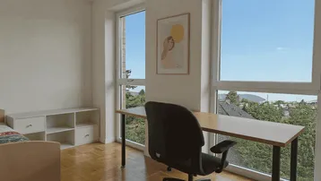 Arbeitszimmer mit großem Fenster, Schreibtisch und Blick ins Grüne.