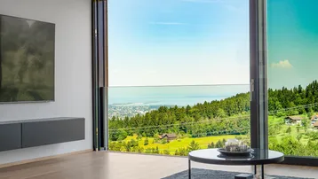 Helles Wohnzimmer mit raumhohen Fenstern und atemberaubendem Blick auf den See und die Landschaft.