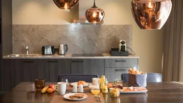 Moderne Küchenzeile mit Essbereich und stilvollen Kupferlampen, ideal für ein gemütliches Frühstück.