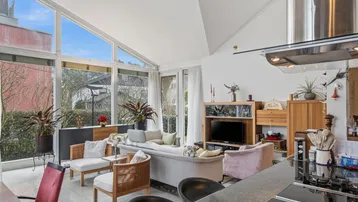 Helles Wohnzimmer mit hohen Decken, großen Fenstern und offenem Übergang zur Küche.
