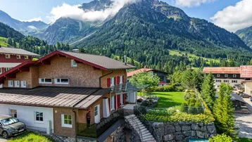 Haus in alpiner Landschaft mit Bergblick und gepflegtem Gartenbereich.