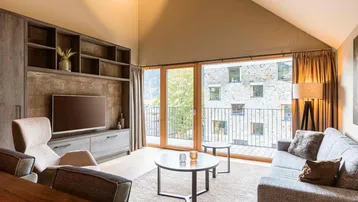 Gemütliches Wohnzimmer mit Sofa, Teppich und Zugang zu einem Balkon mit Bergblick.