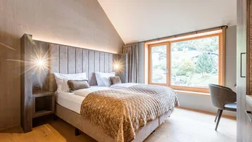 Gemütliches Schlafzimmer mit Holzboden, großem Fenster und Blick auf die grüne Umgebung.