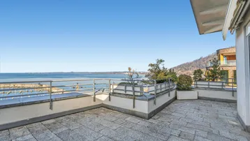 Große Terrasse mit Steinplattenboden, Edelstahlgeländer und weitem Blick auf den See und den Yachthafen.