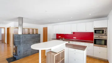 Moderne Küche mit weißen Schränken, roter Rückwand, Kücheninsel und einem Kaminofen.