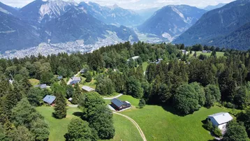 Weitläufige Luftaufnahme einer Siedlung in einer idyllischen Berglandschaft mit bewaldeten Hängen.