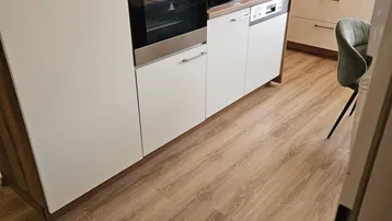 Moderne Einbauküche mit weißen Hochglanzfronten, integrierten Geräten und Holzakzenten.