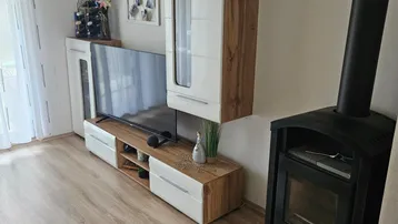 Helles Wohnzimmer mit modernem TV-Möbel, Laminatboden und einem gemütlichen Holzofen.