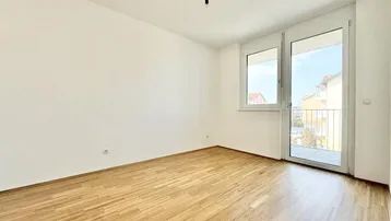 Helles Zimmer mit Holzparkettboden und Zugang zu einem kleinen französischen Balkon.