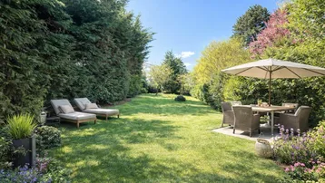 Großer, gepflegter Garten mit Rasenfläche, Liegestühlen und Essbereich unter einem Sonnenschirm.