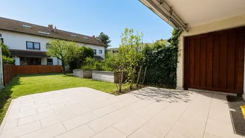 Große gepflasterte Terrasse mit angrenzendem Rasenbereich und Blick auf Nachbargebäude.