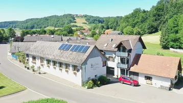 Luftaufnahme eines Gebäudekomplexes mit Solaranlage auf dem Dach in ländlicher Umgebung.