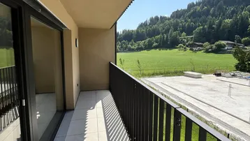 Heller Balkon mit Fliesenboden und Metallgeländer, bietet einen weiten Blick auf grüne Wiesen und Berge.