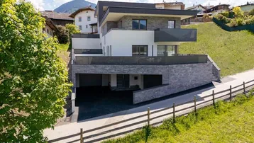 Modernes Wohnhaus mit mehreren Etagen, Balkonen und integrierter Garage in Hanglage.