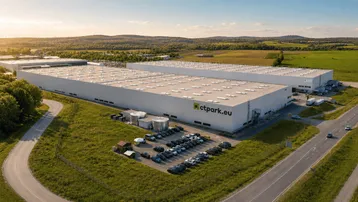 Luftaufnahme eines modernen Industrieparks mit großen weißen Hallen, umgeben von grünen Feldern und Bäumen.