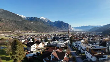 Panoramablick auf eine malerische Stadt im Tal, umgeben von schneebedeckten Bergen unter blauem Himmel.