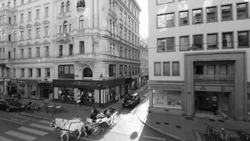 Schwarz-Weiß-Aufnahme einer belebten Stadtstraße mit historischen Gebäuden und einer Pferdekutsche.