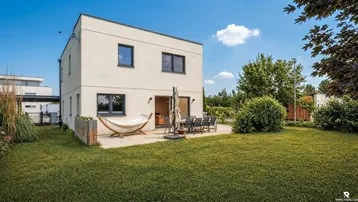 Modernes Einfamilienhaus mit großer Rasenfläche, Terrasse und Hängematte im Garten.