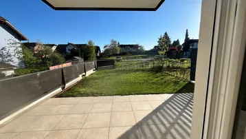 Helle Terrasse mit Fliesenboden und Blick auf den Garten und die umliegende Wohngegend.