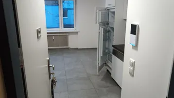 Blick durch die Tür in einen Raum mit Fliesenboden und integrierter Küchenzeile mit Kühlschrank.