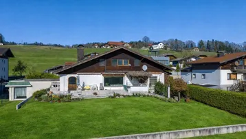 Geräumiges Einfamilienhaus mit großer Rasenfläche, Terrasse und Blick auf die grüne Landschaft.
