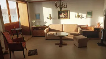 Helles Wohnzimmer mit beiger Couch, klassischem Kronleuchter und Zugang zu einem verglasten Balkon.